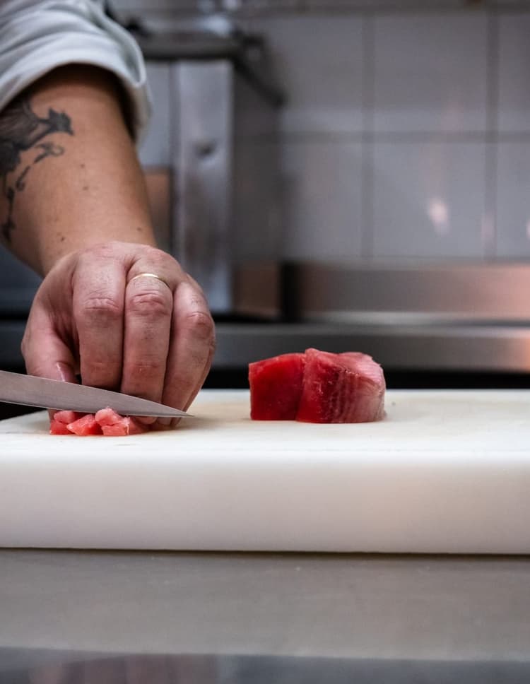 Primer pla d’una mà tallant tonyina fresca.